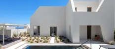 Low-rise white villa under a sunny blue sky with a terrace with planted shrubs and a swimming pool