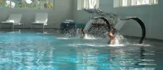 Two people enjoying the water jets at an indoor pool with two loungers in the background