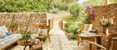 Sunny courtyard with cobbled stone walls, potted plants and greenery, wooden furniture and a neutral sofa 