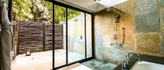Stone-walled bathroom with a bath, shower and windows to an outdoor courtyard with a shower