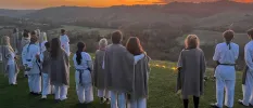 Group stands on a hillside as the sun sets over the mountains in the distance