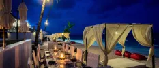 Candelit tables on a beachfront terrace, fronted by a four-poster cabana and daybed draped in white fabric