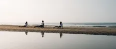 Three people in white practice yoga on the beach under a morning sky