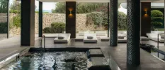 Indoor pool in a room full of pillars, with white modern daybeds and full-length windows
