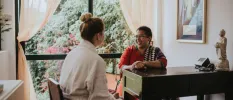 Woman in a robe sits at a wooden desk with a smiling Ayurveda expert