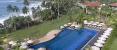 Split-level swimming pool with in-water loungers, surrounded by white parasols and loungers and tropical greenery, with the ocean in the background