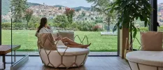 Woman in a robe sitting in a cushioned round chair, overlooking a lawned garden and the hillside town of Fiuggi