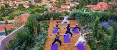 Group enjoy a class on purple yoga mats in a wood-decked garden, overlooking a sea of terracotta rooftops