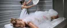 Woman lies on her front covered in foam as a therapist readies a towel behind her