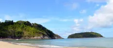Sandy beach lapped by the ocean next to a green hillside and under a blue sky