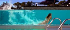 Woman swimming underwater, seen from a glass window from a pool a level down