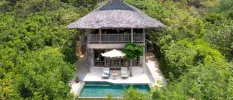 Luxury villa in a tropical forest, with a grey thatched roof, two storeys, a private pool and loungers and an umbrella 