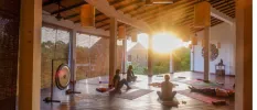 Group in a light-filled studio, with yoga mats and a large gong as the sun rises in the distance