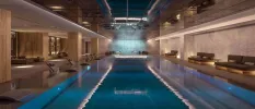 Indoor pool in a marble-walled spa area, with atmospheric lighting and cushioned loungers
