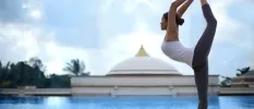 Woman lifts her leg high into the air next to a large swimming pool under a blue cloudy sky