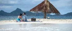 Couple hand in hand on the white sand overlooking the ocean and distant mountains