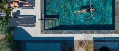 Woman relaxes on her back in a private pool, while a man lounges on the sunbed on the terrace next to it