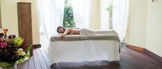 Woman lies on a massage bed half draped in a beige towel with stones on her back