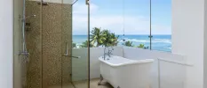 Bathroom with floor-to-ceiling windows with a white bathtub, tiled shower and views over the Indian Ocean