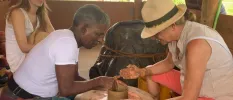 Woman in a straw hat tries pottery with a local instructor, as another woman watches on