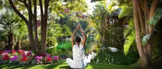 Woman in white with her arms stretched upwards in prayer, overlooking a lake and tropical greenery