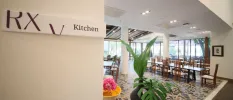 Spacious restaurant with wooden tables and chairs, a stone design floor and a sign reading RXV Kitchen