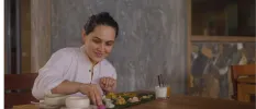 Woman in white sits at a wooden dining table over a plate of food made up of small bites