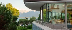 Restaurant with floor-to-ceiling windows and a wraparound balcony overlooking gardens, a lake and mountains