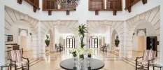 Airy lobby with white walls and archways, high ceilings, dark-wood furniture and potted plants