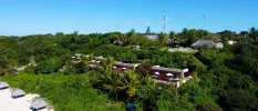Hotel accommodation peeking out of tropical greenery and fronted by a white-sand beach