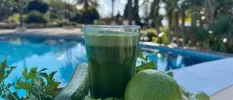 Glass of green juice or smoothie next to a swimming pool