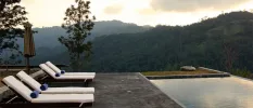 White-cushioned loungers with blue towels overlooking a swimming pool and surrounding mountains and greenery