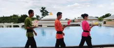 Three staff members in pink, orange and green uniforms carrying colourful drinks past a large pool