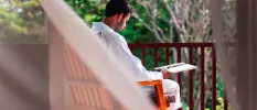 Man in white reads in a wooden chair on a balcony