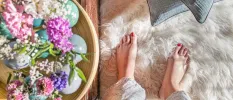 Woman with red painted toenails sinks her feet into a white fur rug next to a table with flowers