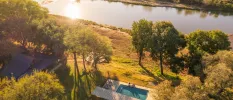 Swimming pool as seen from above, surrounded by greenery and with a river in the background