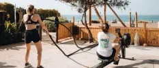 Two ladies in active wear working out on a rower and with ropes overlooking the sea