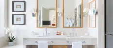Modern bathroom with twin sinks, two wooden mirrors, black framed photos, a white flower and twin robes reflected in the mirror