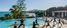 Group in active wear practice yoga on a sunny terrace next to a pool with sea views
