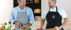 Two smiling men in aprons chop vegetables in a workshop as part of a cooking class