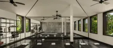 Airy studio with ceiling fans, white walls and dark-wood floors, set up for a class with black yoga mats and white towels