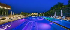 Swimming pool surrounded by white umbrellas and loungers, lit up under a darkening sky