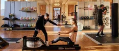 Woman on a gym machine while an instructor assesses her in a gym with chandeliers