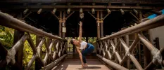 Woman in blue leggings and a white sports bra practices yoga on a wooden pavilion walkway