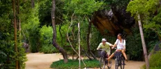 Two people smile while riding bikes through a tropical forest