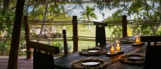 Outdoor restaurant terrace with a lagoon view, thatched roof, wooden tables and rattan placemats with candle centrepieces