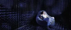 Woman relaxes in a bean bag chair in a dark room filled with LED lights on the wall, ceiling and floor