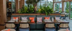 Tables with placemats and utensils among orange and white patterned cushions and lush greenery