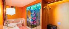Bathroom with a hanging chandelier, tiled pink floor and a shower with a colourful mermaid mural painted all over 