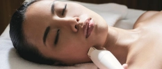Woman lies on a message bed and having a facial treatment done with derma pen